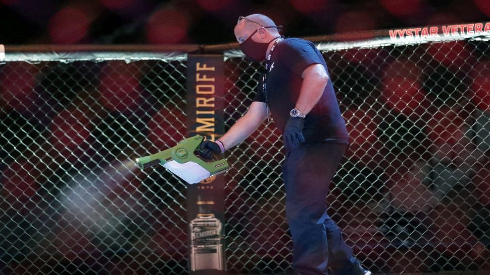 A worker uses a sanitizing spray in the octagon between bouts at UFC 249 in Jacksonville.  (AP Photo/John Raoux)