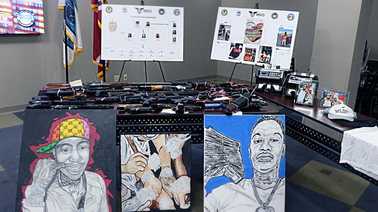 Displayed are firearms, drawings and other items seized by authorities. Also pictured is the "55 Boyz" organizational chart.  (Spectrum News/Elizabeth Barmeier)