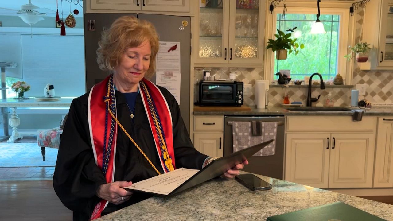 college masters degree holder, in her graduation gown, admires her diploma in a bathroom