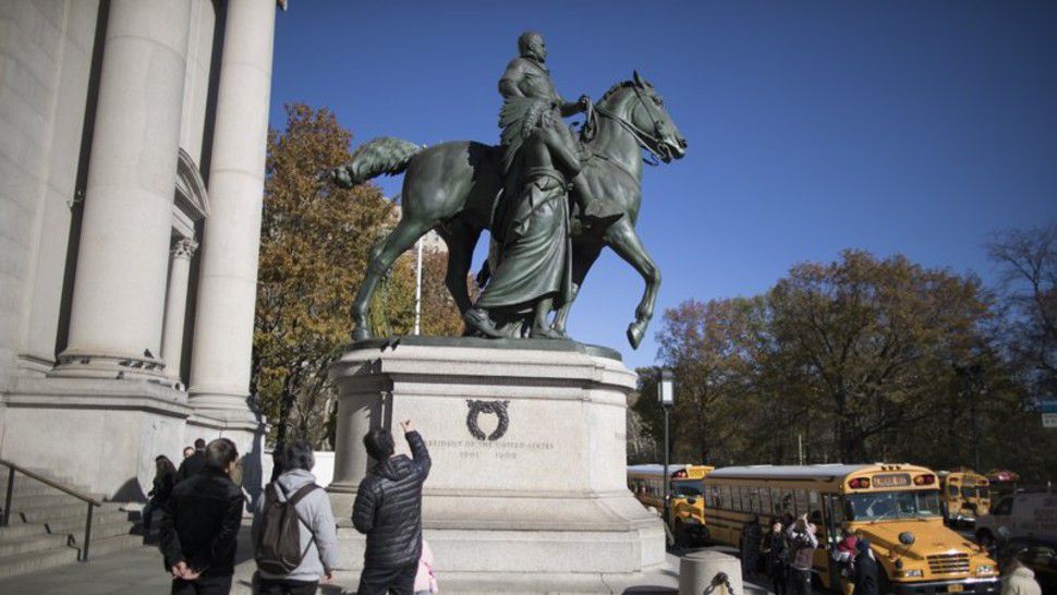 In this Nov. 17, 2017 file photo, visitors to the American Museum of Natural History in New York look at a statue of Theodore Roosevelt, flanked by a Native American man and African American man. The statue will be coming down after the museum's proposal to remove it was approved by the city (AP Photo/Mary Altaffer, File)