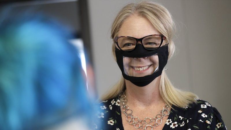 In this June 3, 2020, photo, Chris LaZich, of Fleet Science Center, wears a mask with a window as she talks with Delpha Hanson in San Diego. Face coverings to curb the spread of the coronavirus are making it hard for people who read lips to communicate. That has spurred a slew of startups making masks with plastic windows to show one's mouth. The companies are getting inundated with orders from family and friends of deaf people, people helping English learners see the pronunciation of words, and even hospitals that want their patients to be able to see smiles. (AP Photo/Gregory Bull)