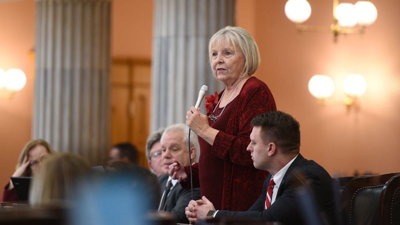 A woman stands in a room of people with a microphone