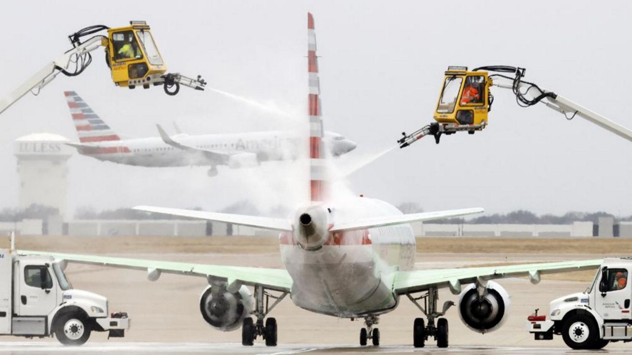 Aerial crews deice an American Airlines jet before it can take off as another lands at Dallas/Fort Worth International Airport, Wednesday, Feb. 23, 2022, in Dallas. Light precipitation was falling as temperatures were in the mid 20's. (Tom Fox/The Dallas Morning News via AP)