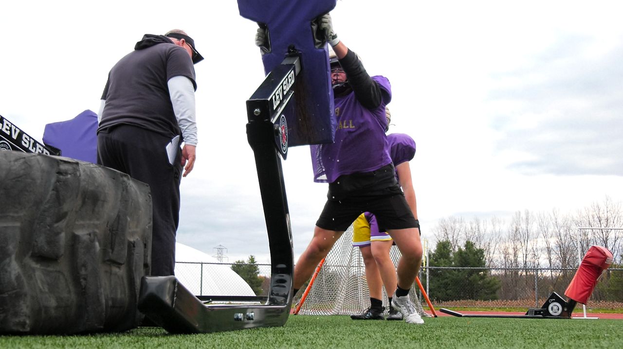 cba albany player, with coach watching on cloudy day, hits a blocking sled