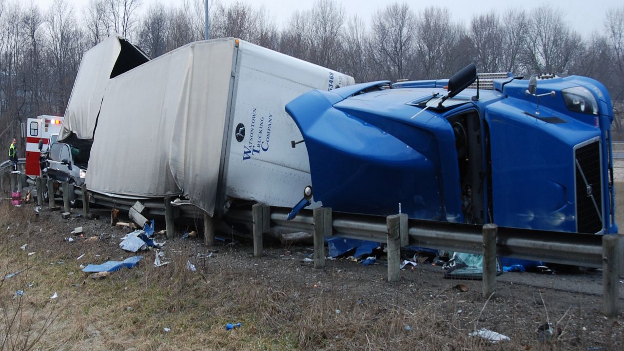 a crashed truck tipped over on its side against a guardrail