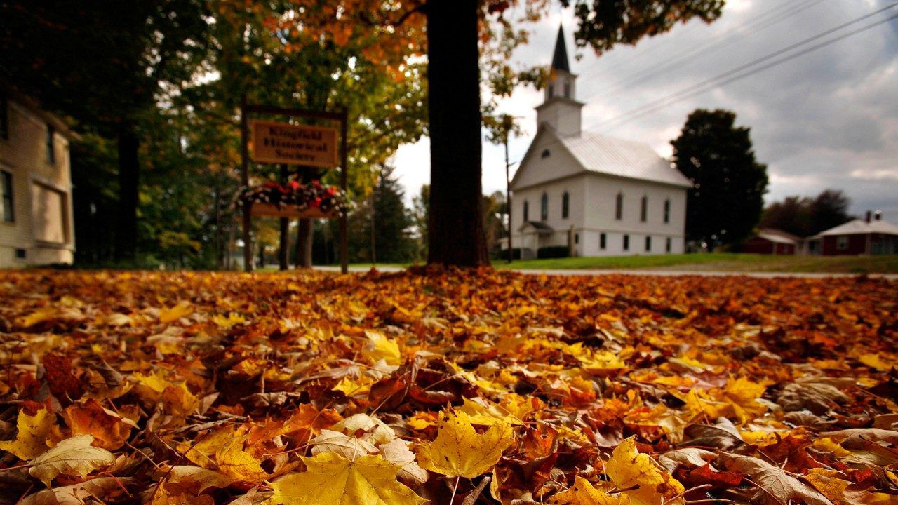 Fallen maple leaves carpet a lawn across the street from the First Baptist Church of Kingfield, Maine 