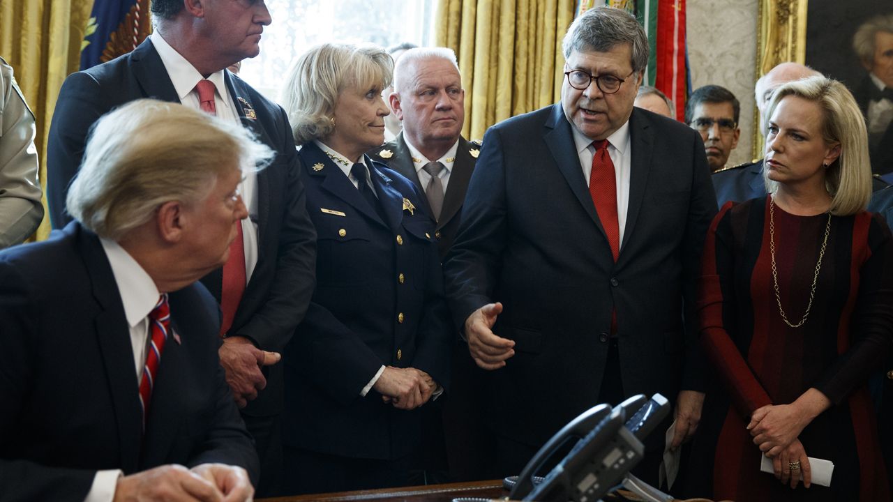 Attorney General Bill Barr speaks to President Donald Trump before he signs the first veto of his presidency in the Oval Office of the White House, Friday, March 15, 2019, in Washington. Trump issued the first veto, overruling Congress to protect his emergency declaration for border wall funding. (AP Photo/Evan Vucci)