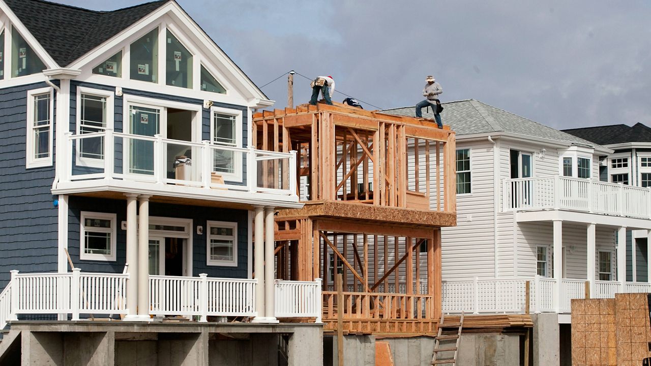 In this Oct. 15, 2014, file photo, carpenters work on a new house under construction, center, between other new homes in the Breezy Point neighborhood of the Queens borough of New York. Following Superstorm Sandy, new houses there were being built on elevated foundations to raise the buildings above anticipated flood waters. (AP Photo/Mark Lennihan)