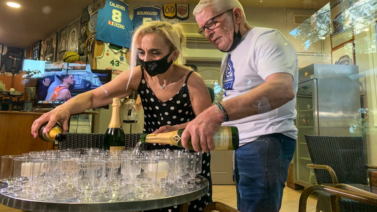 Coffee shop owner Yiannis Tzikas and his wife Kaiti Drimba pour champagne into plastic glasses after the Milwaukee Bucks win the NBA title, in the Sepolia district of Athens. (AP Photo/Derek Gatopoulos)
