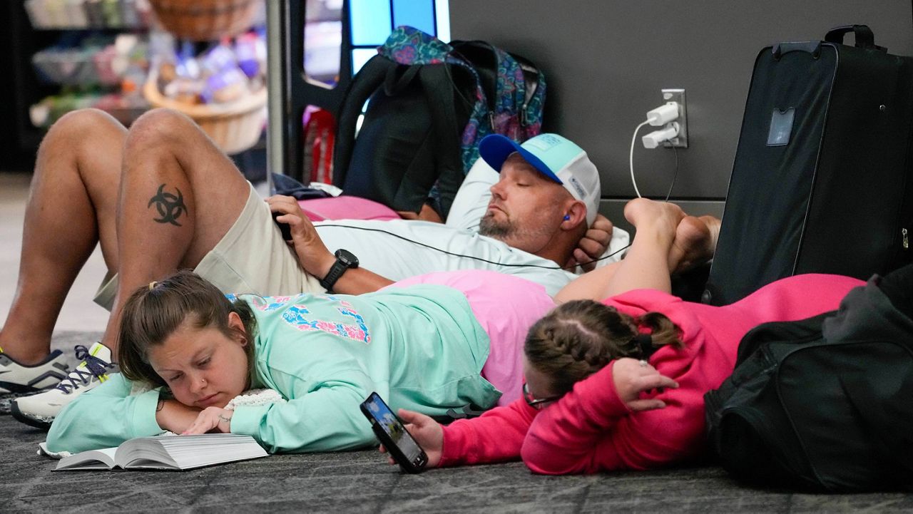 Travelers use their electronic devices while lying on the floor of the departures area of Terminal B at LaGuardia Airport, Tuesday, June 27, 2023, in New York. (AP Photo/Mary Altaffer)