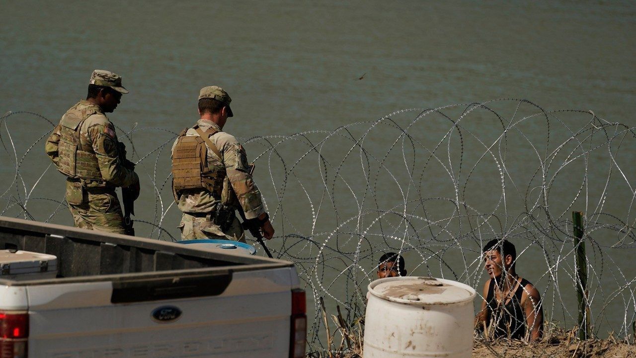 Guardsmen talk with migrants trying to cross the Rio Grande from Mexico into the U.S. near in Eagle Pass, Texas, Tuesday, July 11, 2023. (AP Photo/Eric Gay)