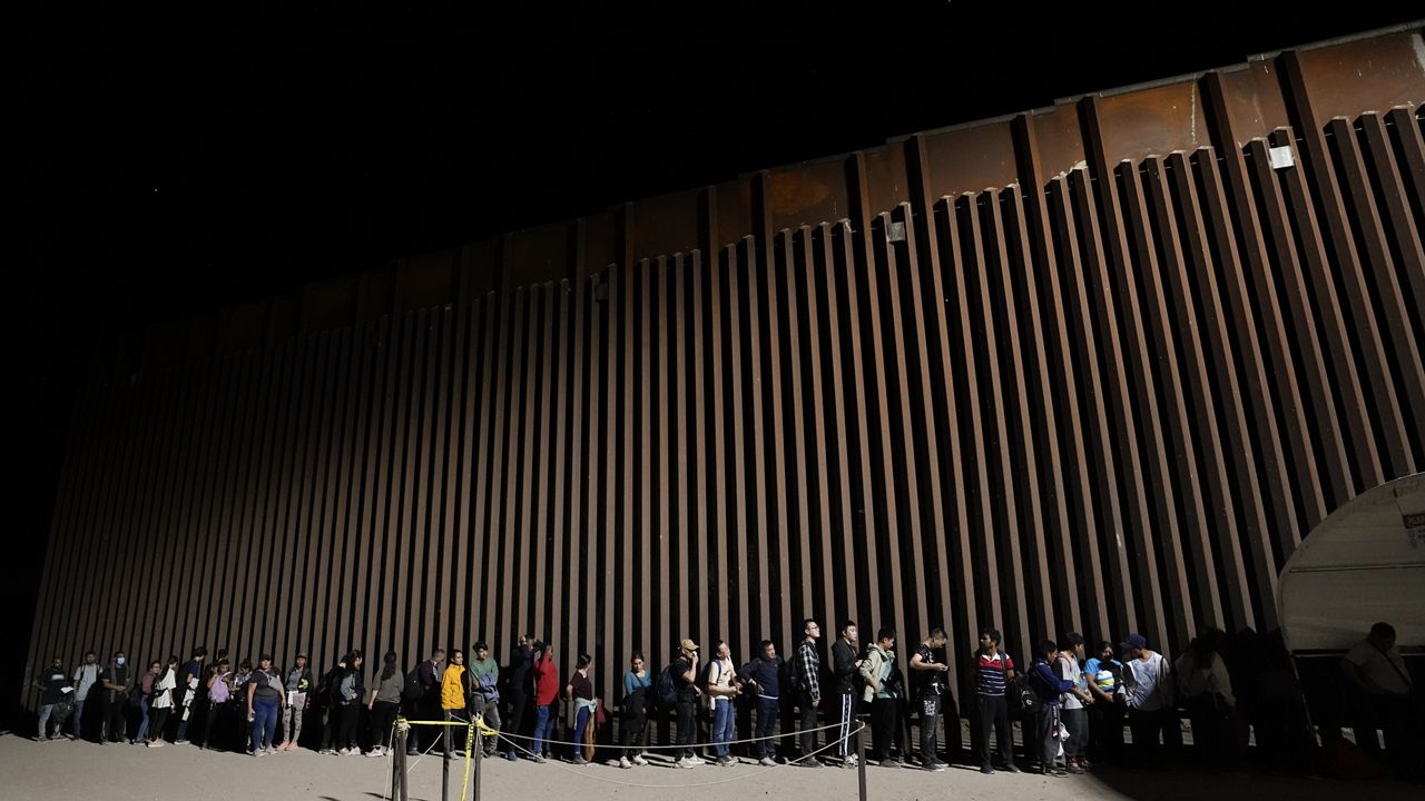 People line up against a border wall as they wait to apply for asylum after crossing the border from Mexico Tuesday, July 11, 2023, near Yuma, Arizona. (AP Photo/Gregory Bull)