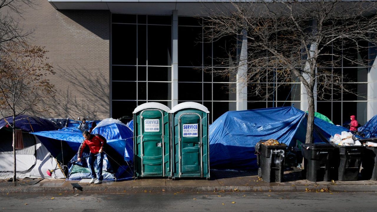 A migrant man sweeps the sidewalk of leaves and melting snow in a small tent community, Wednesday, Nov. 1, 2023, near a Northside police station in Chicago. AP Photo/Charles Rex Arbogast)