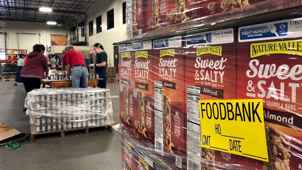 A pallet of food awaits processing as volunteers work in the background to label cans of beans for redistribution at Roadrunner Food Bank in Albuquerque, N.M., Thursday, May 7, 2020. (AP Photo/Susan Montoya Bryan, File)