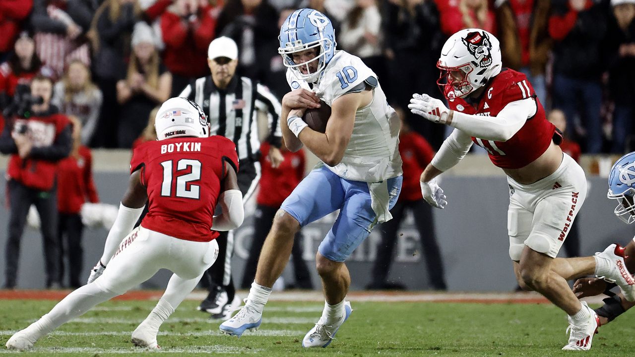 North Carolina's Drake Maye (10) tries to run the ball between North Carolina State defensive back Devan Boykin (12) and linebacker Payton Wilson (11) during the first half of an NCAA college football game in Raleigh, N.C., Saturday, Nov. 25, 2023. (AP Photo/Karl B DeBlaker)