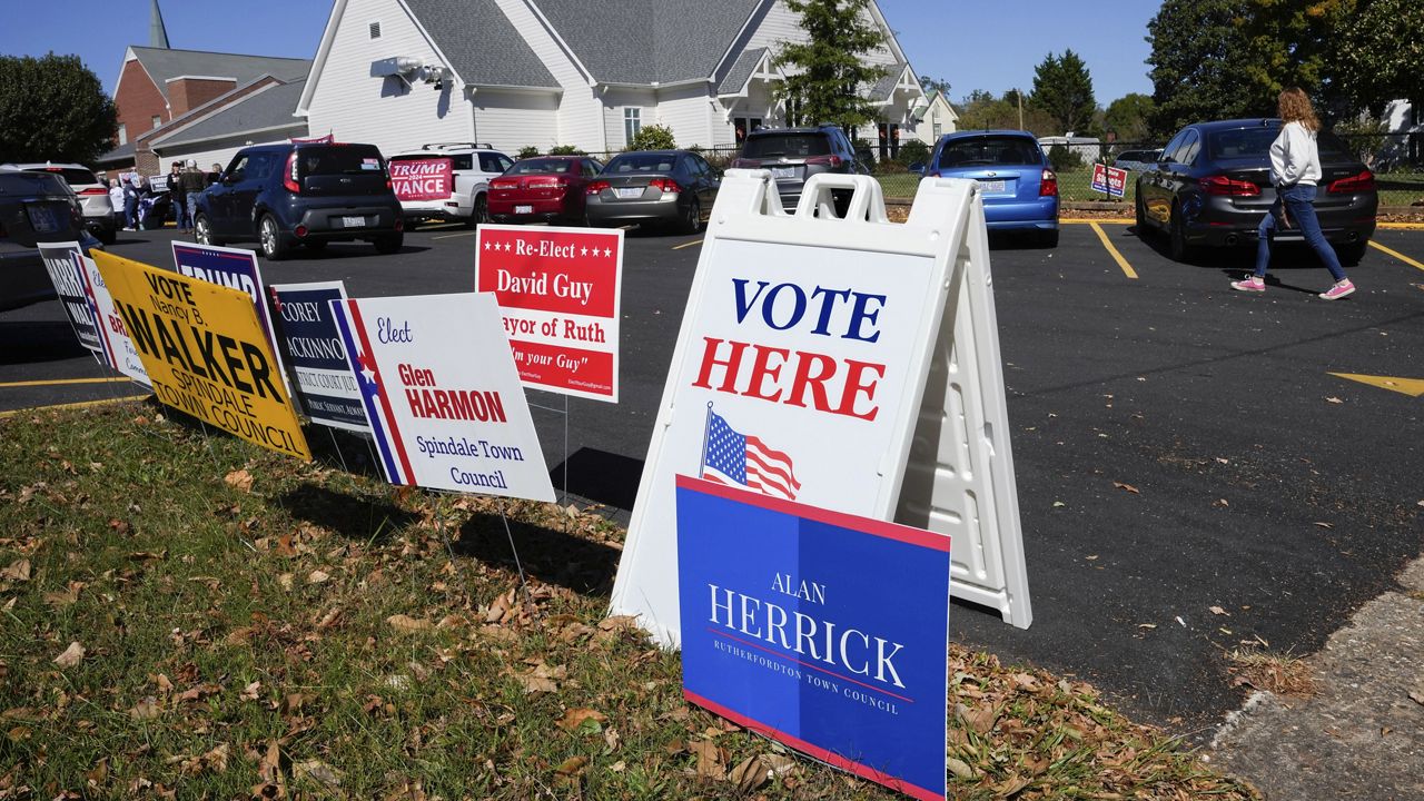 A Vote Here sign is posted amongst political signs as people arrive to vote at the Rutherford County Annex Building, an early voting site, Thursday, Oct. 17, 2024, in Rutherfordton, N.C. (AP Photo/Kathy Kmonicek)