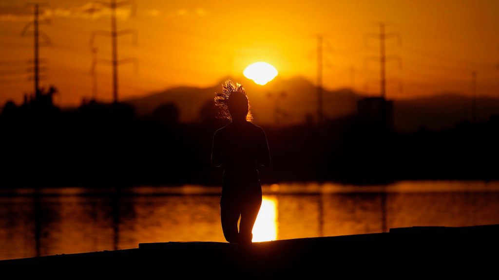 A runner jogs along Tempe Town Lake at sunrise, Wednesday, July 12, 2023 in Tempe, Ariz. (AP Photo/Matt York)