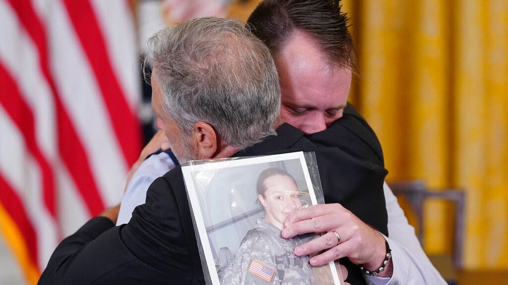 Activist and entertainer Jon Stewart hugs Sri Benson, husband of Katie Benson who served in Kuwait and died of mesothelioma, as they arrive to attend an event where President Joe Biden will sign the 