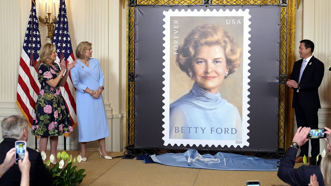 Susan Ford Bales, second from left, daughter of former first lady Betty Ford, first lady Jill Biden, left, and President and CEO of the Hazelden Betty Ford Foundation Dr. Joseph Lee, right, watch in the East Room of the White House in Washington, Wednesday, March 6, 2024, during an unveiling of a new U.S. Postal Service stamp honoring former first lady Betty Ford. (AP Photo/Susan Walsh)