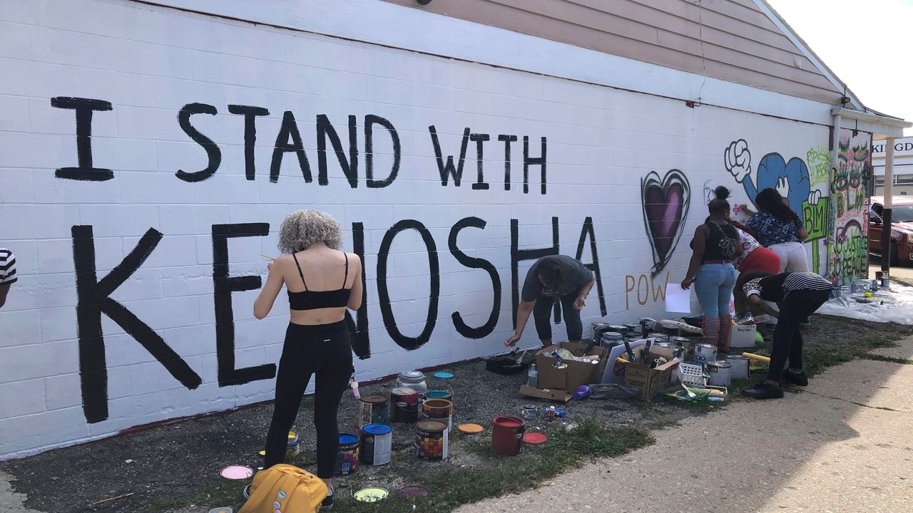 David Sanchez, 66, a long-time Kenosha, Wis., resident, watches volunteers paint murals on boarded-up businesses on Sunday, Aug. 30, 2020. The businesses were affected by recent violent protests following the police shooting of Jacob Blake. (AP Photo/ Russell Contreras)