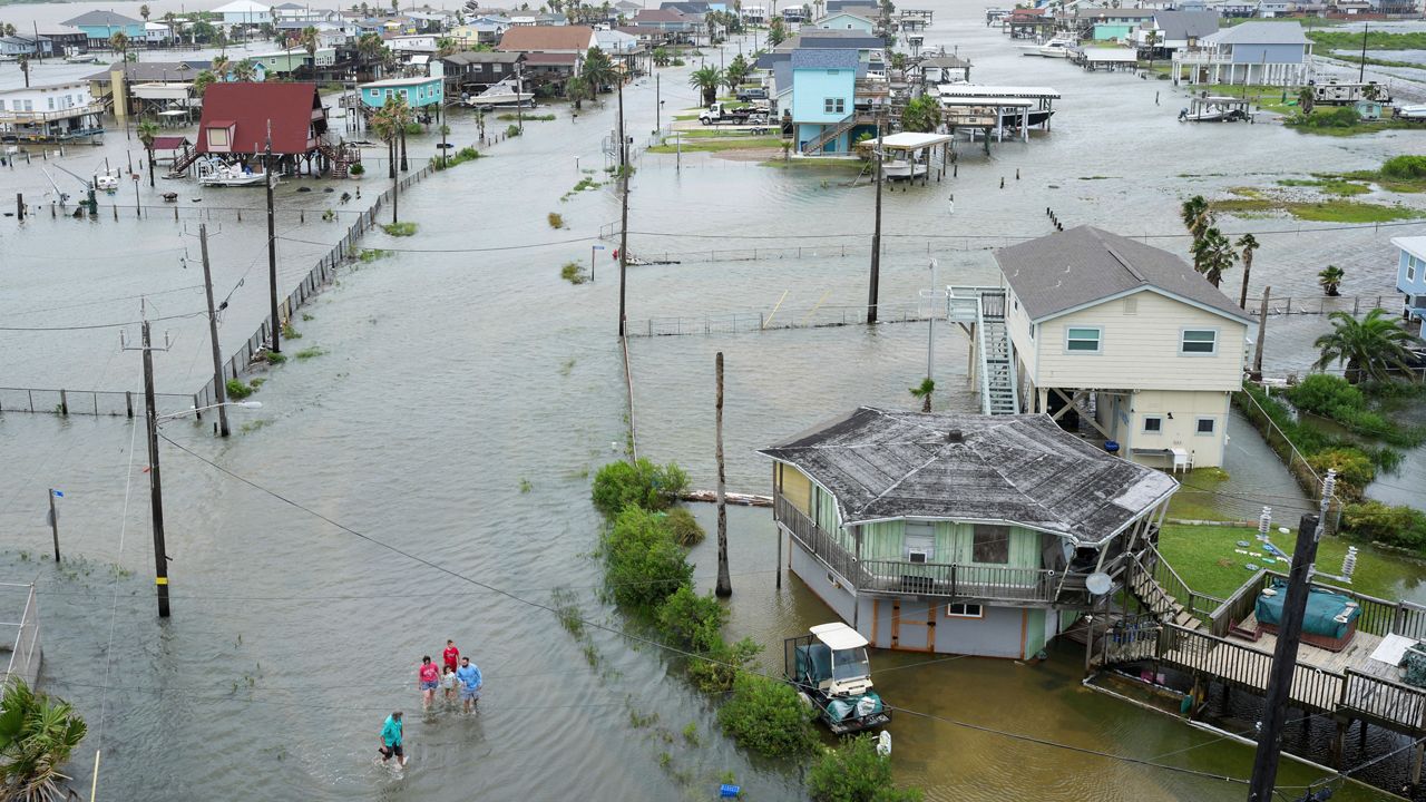 Joseph Canzanella, left, greets members of the Vise family as he walks through the storm surge from Tropical Storm Alberto to get to work Wednesday, June 19, 2024, in Surfside Beach, Texas. "This ain't the first time I've had to do this, and it won't be the last," Canzanella said. ( Jon Shapley/Houston Chronicle via AP)