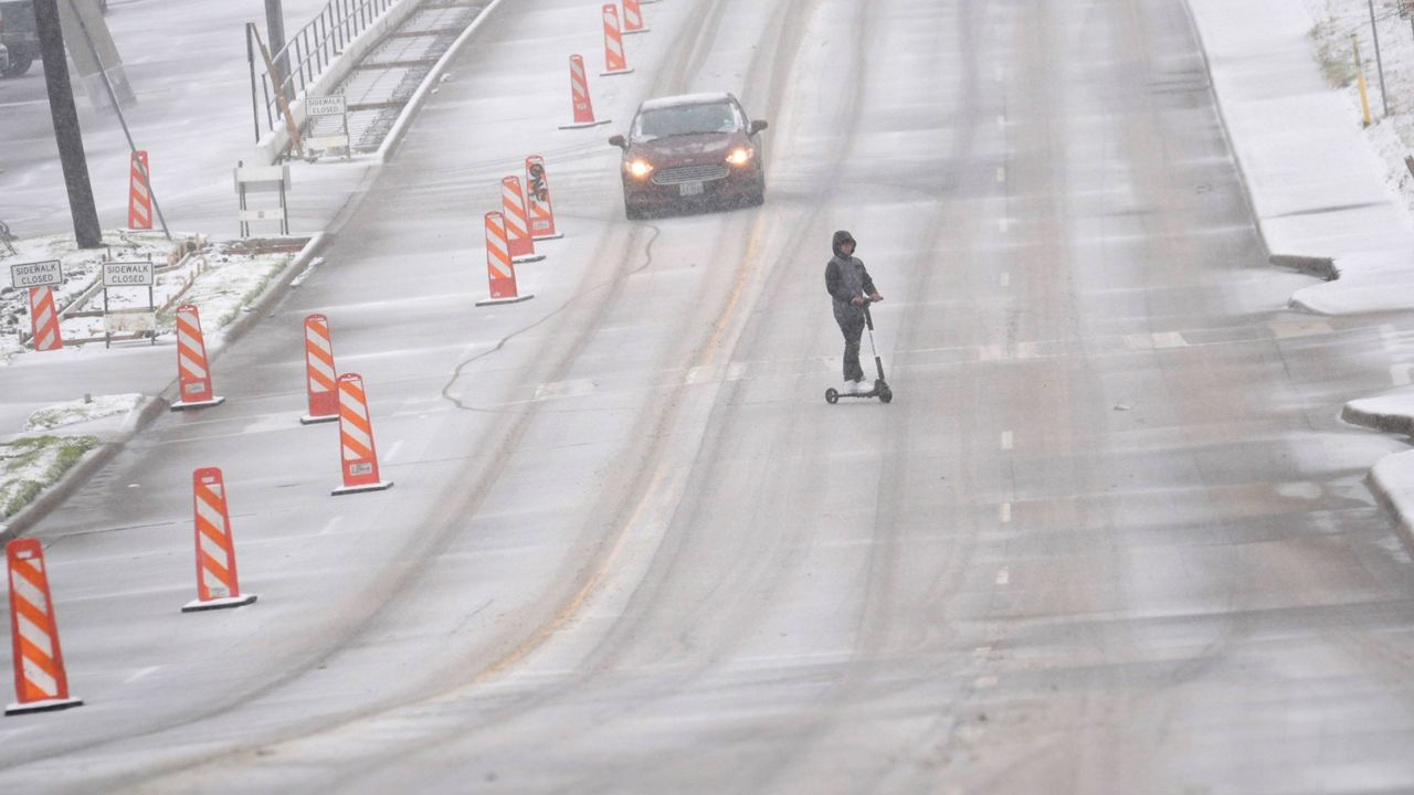 Snow falls as a car and a scooter make their way along a street Thursday, Jan. 9, 2025, in Dallas. (AP Photo/LM Otero)