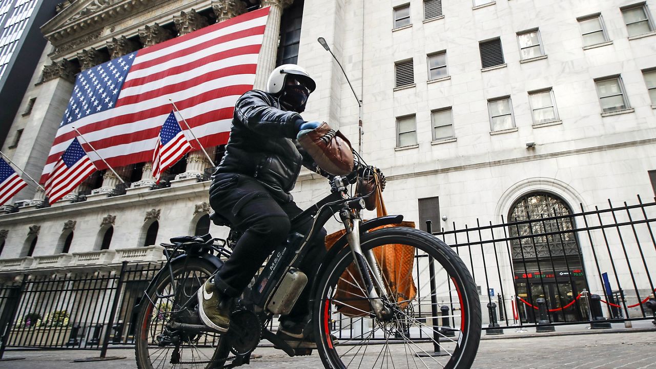 A delivery worker rides his electric bicycle past the New York Stock Exchange, March 16, 2020, in New York. (AP Photo/John Minchillo)