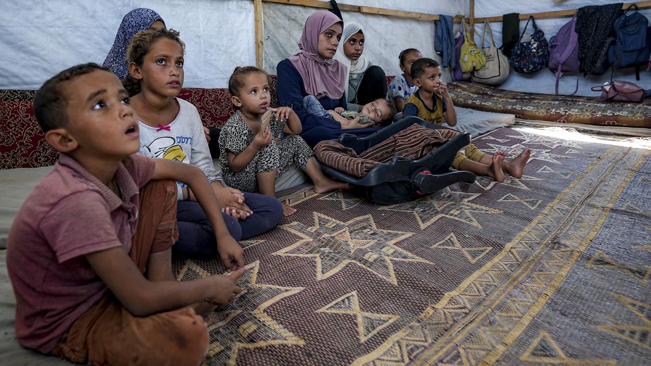 Displaced infant Abdel-Rahman Abu El-Jedian, 11-month-old, who suffers from polio, is carried by his mother, center, at a makeshift tent camp in Deir al-Balah, central Gaza Strip, Tuesday, Aug. 27, 2024. (AP Photo/Abdel Kareem Hana)