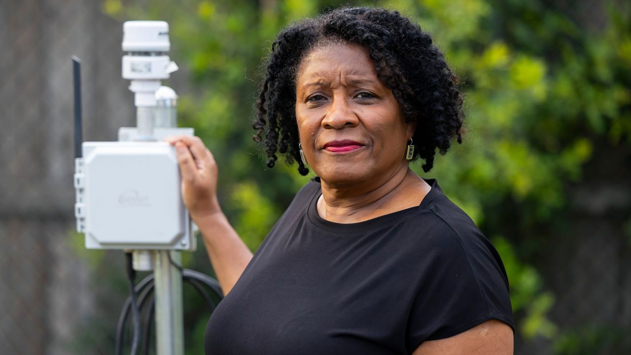 Bridgette Murray poses next to an air quality monitor in the Pleasantville area of Houston, Saturday, Aug. 17, 2024. (AP Photo/Annie Mulligan)