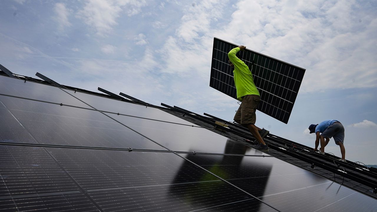 Nicholas Hartnett, owner of Pure Power Solar, carries a panel as he and Brian Hoeppner, right, install a solar array on the roof of a home in Frankfort, Ky., July 17, 2023. (AP Photo/Michael Conroy