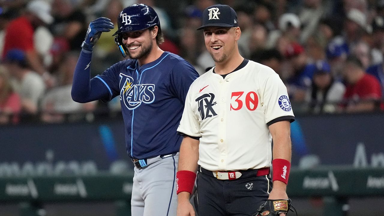 Texas Rangers first baseman Nathaniel Lowe (30) and his brother Tampa Bay Rays' Josh Lowe, left, laugh at first base after Josh singled during the sixth inning of a baseball game in Arlington, Texas, Friday, July 5, 2024. (AP Photo/LM Otero)