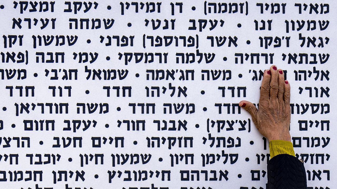 A woman touches the wall with names of fallen soldiers during Israel's annual Memorial Day for the fallen soldiers who died in the nation's conflicts and victims of nationalistic attacks at the Armored Corps memorial site in Latrun, Israel, Monday, May 13, 2024. (AP Photo/Ariel Schalit)