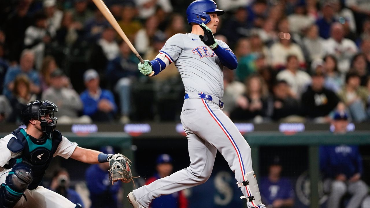 Texas Rangers' Nathaniel Lowe follows through on an RBI single to score Wyatt Langford as Seattle Mariners catcher Cal Raleigh looks on during the eighth inning of a baseball game Thursday, Sept. 12, 2024, in Seattle. (AP Photo/Lindsey Wasson)