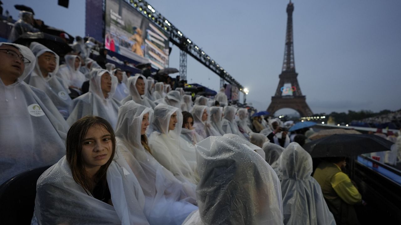 Spectators sit in the rain in Paris, France, during the opening ceremony of the 2024 Summer Olympics, Friday, July 26, 2024. (AP Photo/Robert F. Bukaty)