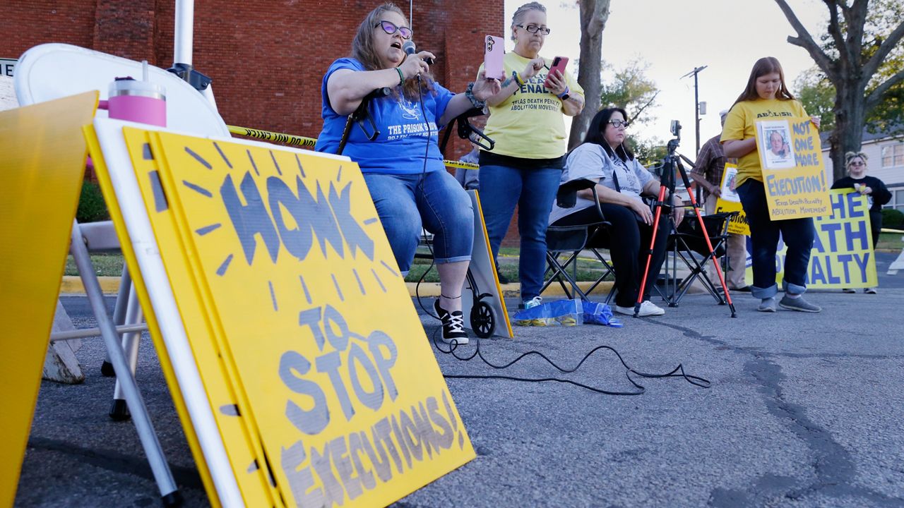 Dani Allen, center left with microphone, an anti-death penalty advocate, speaks during a protest outside the prison where Robert Roberson is scheduled for execution at the Huntsville Unit of the Texas State Penitentiary, Thursday, Oct. 17, 2024, in Huntsville, Texas. (AP Photo/Michael Wyke)