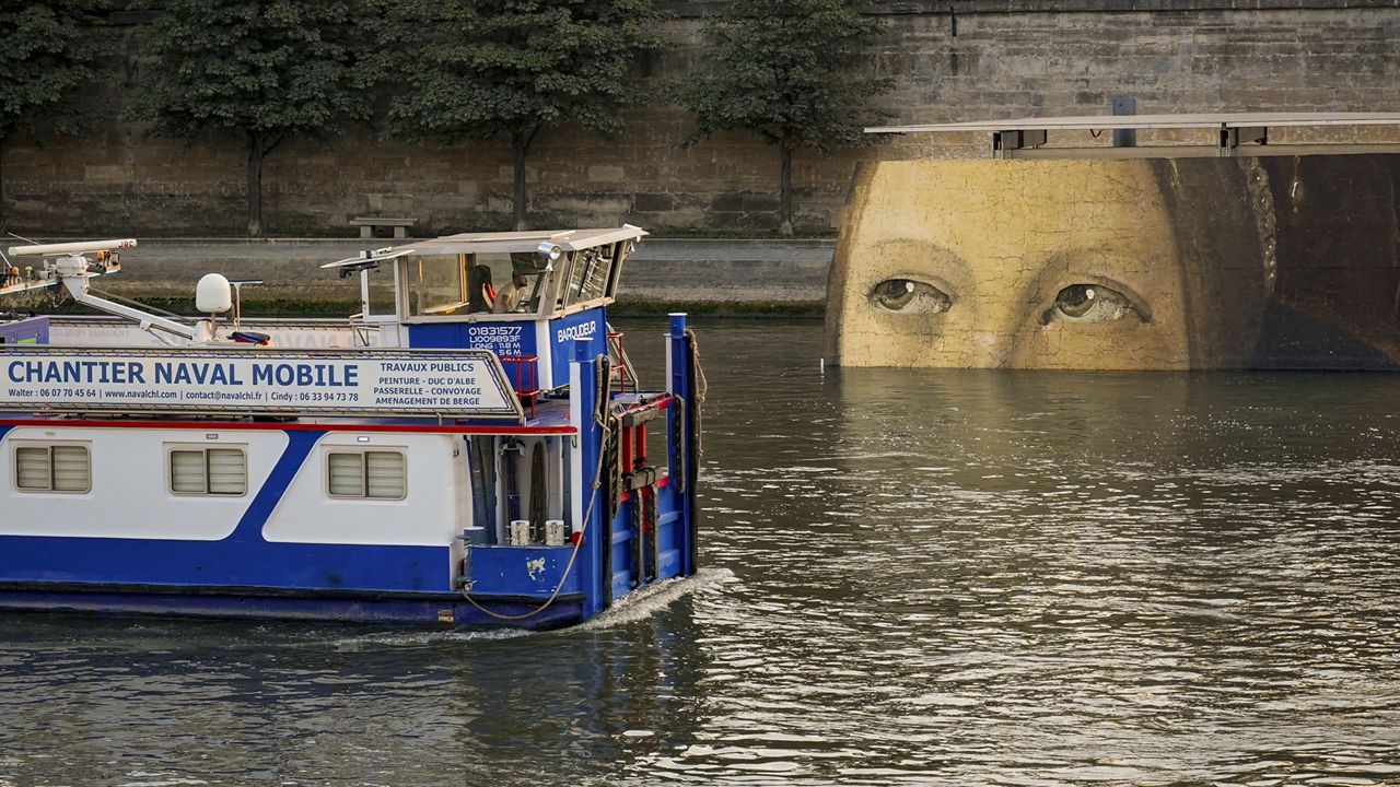 A ship sails past reproductions of artworks decorating the banks of the River Seineat the 2024 Summer Olympics, Tuesday, July 30, 2024, in Paris, France. (AP Photo/ Dar Yasin)