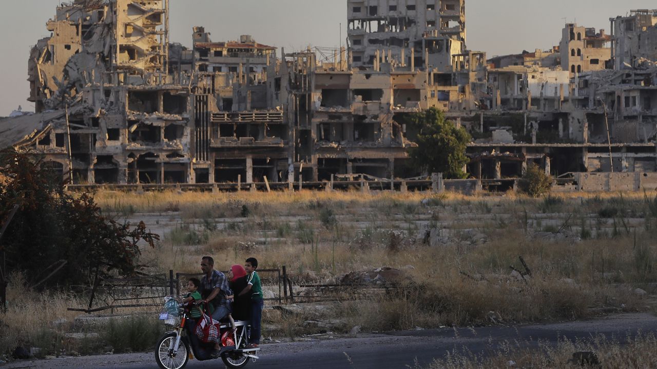 People ride their motorcycle by damaged buildings in the old town of Homs, Syria, Aug. 15, 2018. (AP Photo/Sergei Grits, File)