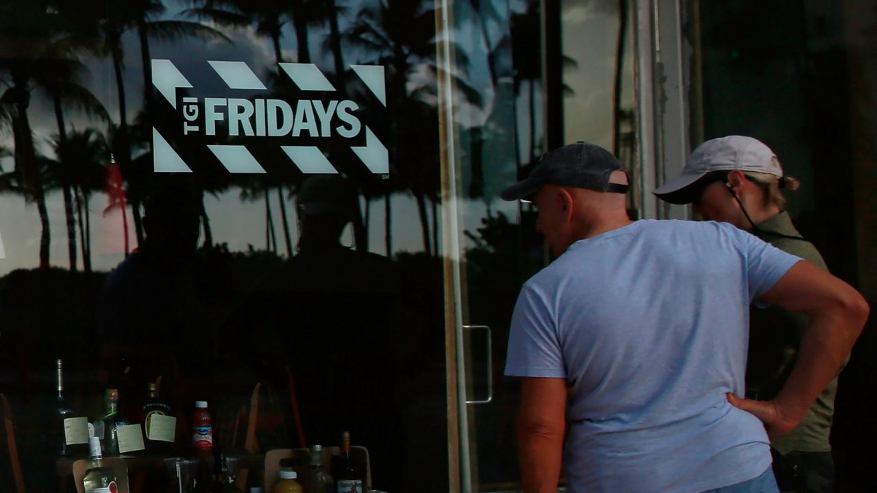 People peek into a window of a TGI Friday's restaurant to see what they are serving to-go on Wednesday, March 25, 2020, in Miami Beach, Fla. (AP Photo/Brynn Anderson, File)