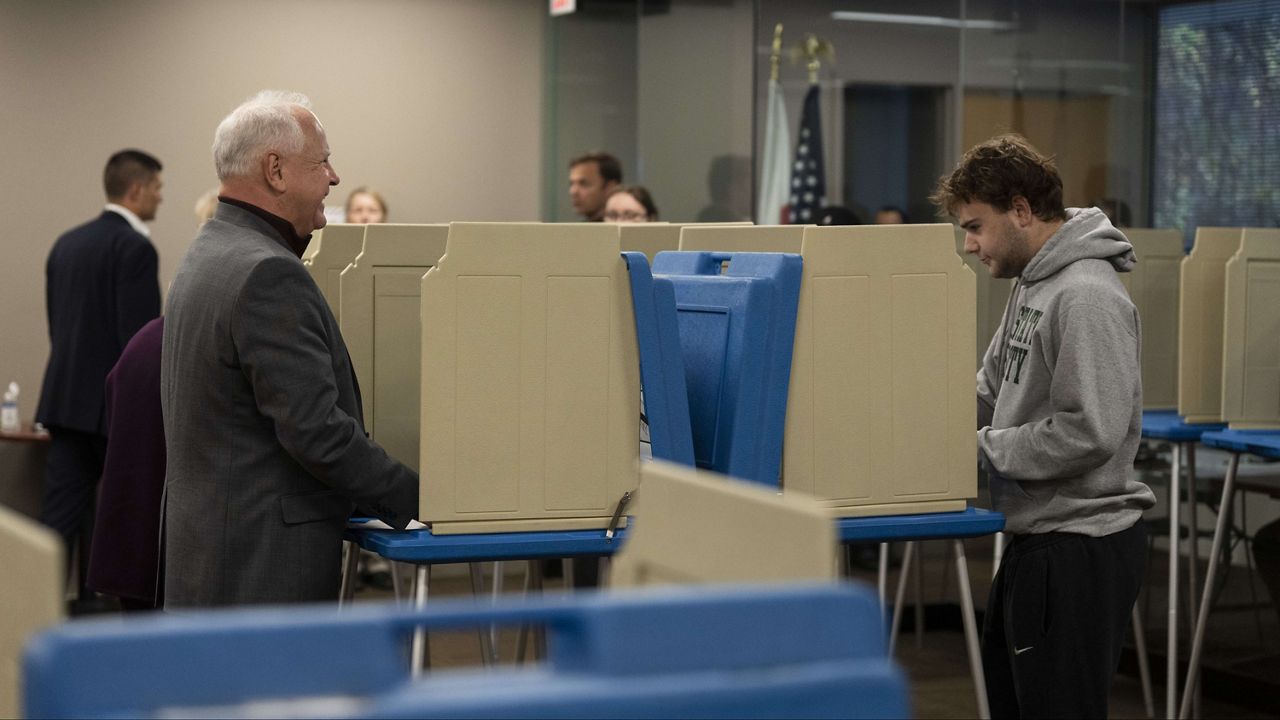 Minnesota Gov. and Vice Presidential candidate Tim Walz, left, chats with his son, Gus Walz, as they cast their ballots during early voting at Ramsey County Elections in St. Paul, Minn., on Wednesday, October 23, 2024. (Renée Jones Schneider/Star Tribune via AP)