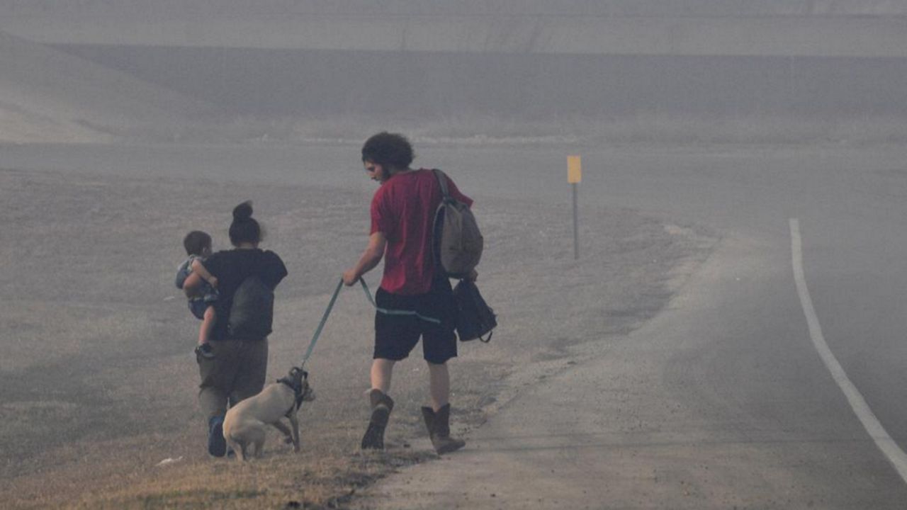 A family walks through smoke down the Arnold Blvd. frontage road after evacuating the Continental Villa mobile home park in Abilene, Texas Thursday March 17, 2022. A quickly-moving grass fire was heading that way, prompting officials to order the evacuation. (Ronald W. Erdrich/The Abilene Reporter-News via AP)