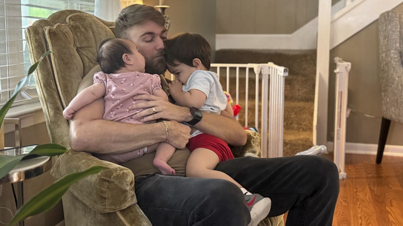 U.S. Marine Corps veteran Adrian Clouatre holds his 3-month-old daughter Lyn and his nearly two old son Noah at their home in Baton Rouge, La. on Tuesday, June 17, 2025. (AP Photo/Stephen Smith)