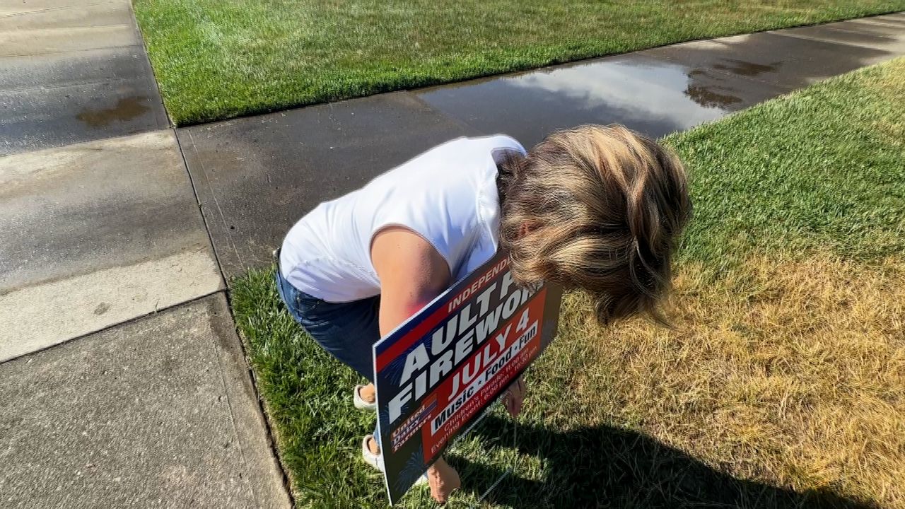 Anne Sesler places a sign for the fireworks at Ault Park.