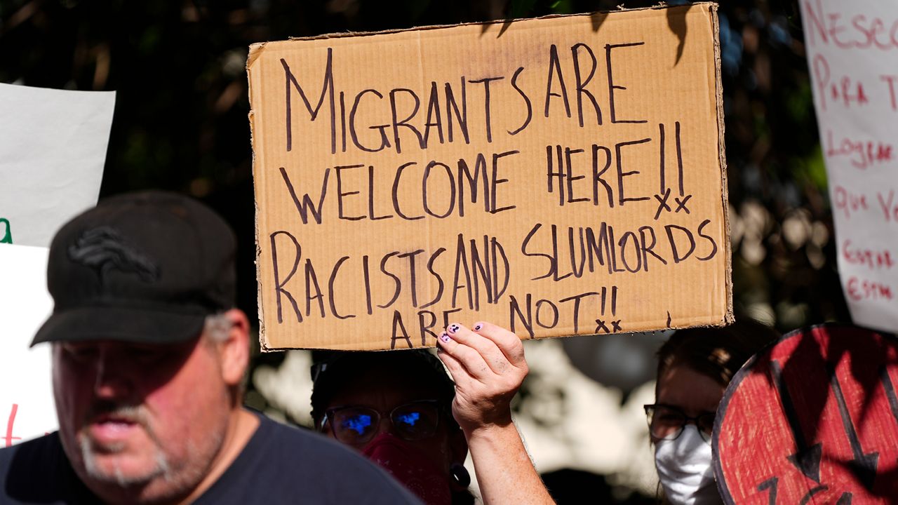 A protester holds up a placard during a rally staged by the East Colfax Community Collective to address chronic problems in the apartment buildings occupied by people displaced from their home countries in central and South America Tuesday, Sept. 3, 2024, in Aurora, Colo. (AP Photo/David Zalubowski)