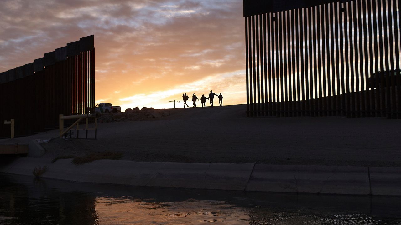 Photo of people walking in between a gap in a border wall (Associated Press)