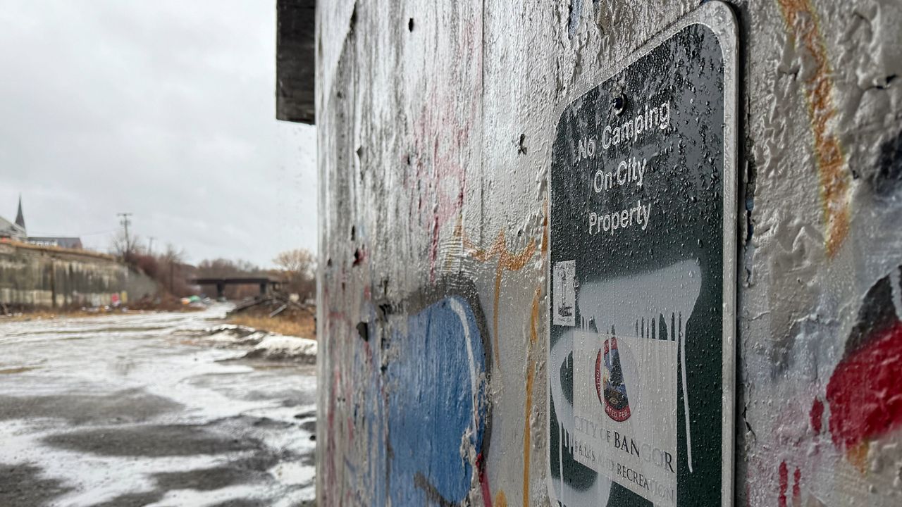 A Bangor ‘no camping’ sign covered with graffiti hangs under the Penobscot River Bridge. (Spectrum News/David Ledford)