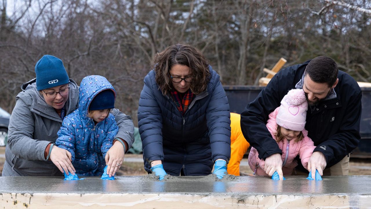 Annie Colaluca, executive director of Early Learning and Family Services for the Bath Area Family YMCA, joins two children of BIW shipbuilders as they press handprints into a cement slab that will be used for the new childcare center’s bicycle rack. She is joined, from left, by Sophia, 4, and her mother Ellen McIver, BIW senior specialist strategic planning, and Emilie, 3, and her father, BIW Manufacturing Director Brandon Glazier. (Contributed photo via Bath Iron Works)