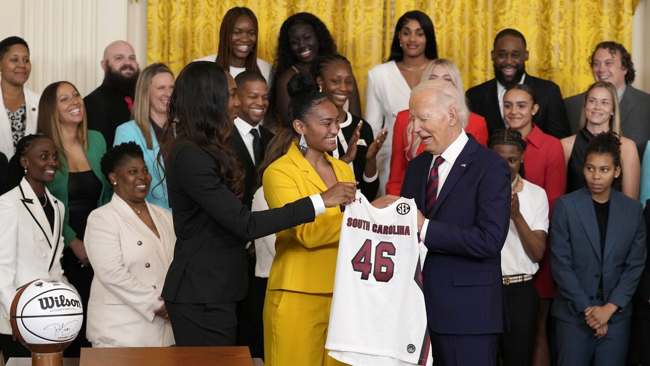 President Joe Biden, right, holds up a jersey that was presented to him by University of South Carolina Women's basketball team members Bree Hall, left, and Te-Hina Paopao, center, during an event in the East Room of the White House in Washington, Tuesday, Sept. 10, 2024, to celebrate their 2023-2024 NCAA championship season. (AP Photo/Susan Walsh)