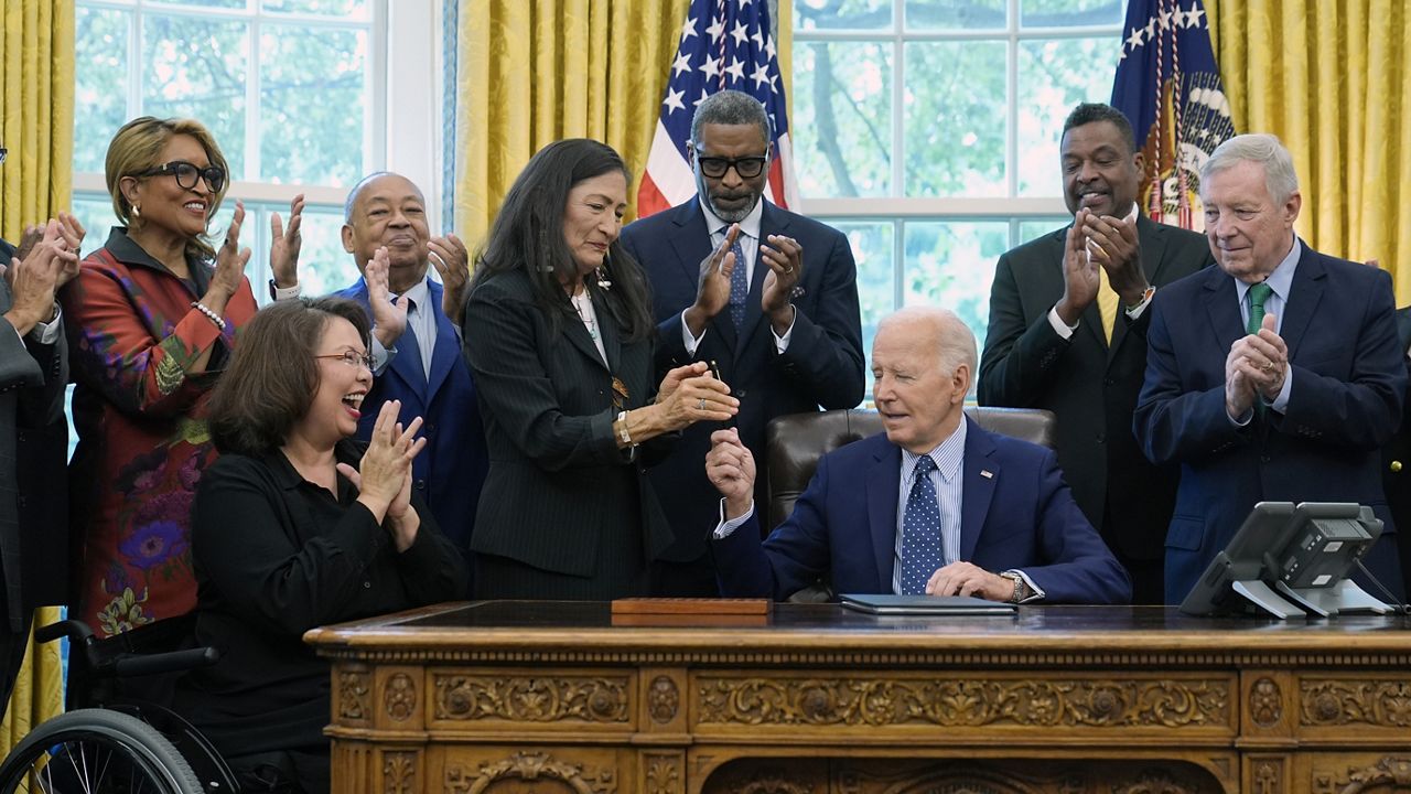 President Joe Biden, who is joined by civil rights leaders, community members, and elected officials, hands Interior Secretary Deb Haaland, fourth from left, the pen he used to sign a proclamation in the Oval Office of the White House in Washington, Friday, Aug. 16, to designate the Springfield 1908 Race Riot National Monument. hugs Sen. Tammy Duckworth, D-Ill., second from left, reacts. (AP Photo/Susan Walsh)