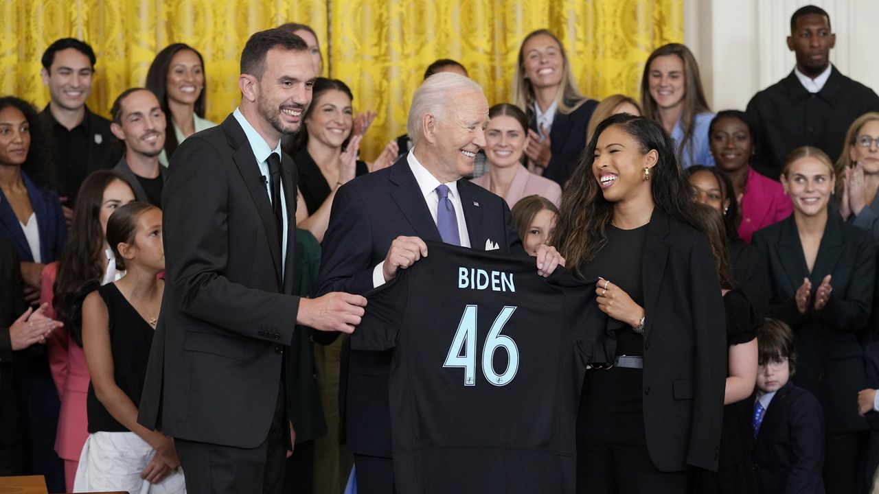 President Joe Biden, center, is presented with a team jersey from NJ/NY Gotham FC head coach Juan Carlos Amoros, left, and teammate Midge Purse, right, during an event in the East Room of the White House in Washington, Monday, Sept. 23, 2024, to welcome the NJ/NY Gotham FC and celebrate their 2023 NWSL championship. (AP Photo/Susan Walsh)