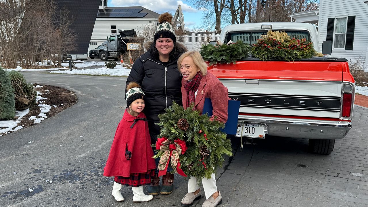 Maine Gov. Janet Mills is presented with a wreath from with Heidi Watson and Watson's daughter, Elowen, 3. (Spectrum News/Matthew Jaroncyk)